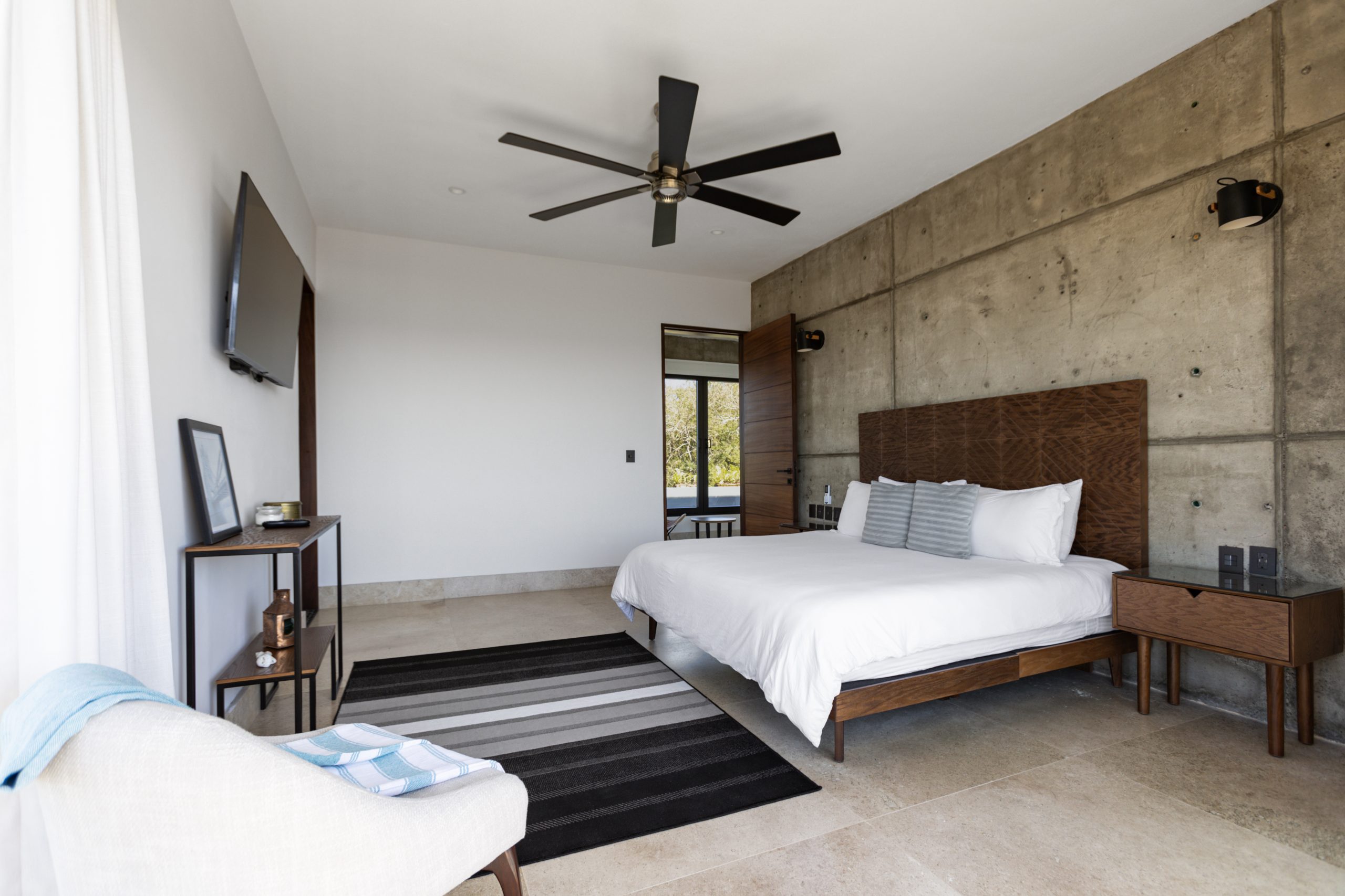 edroom with panoramic ocean views through large corner windows, light-colored curtains, and a cozy chair with a blanket.