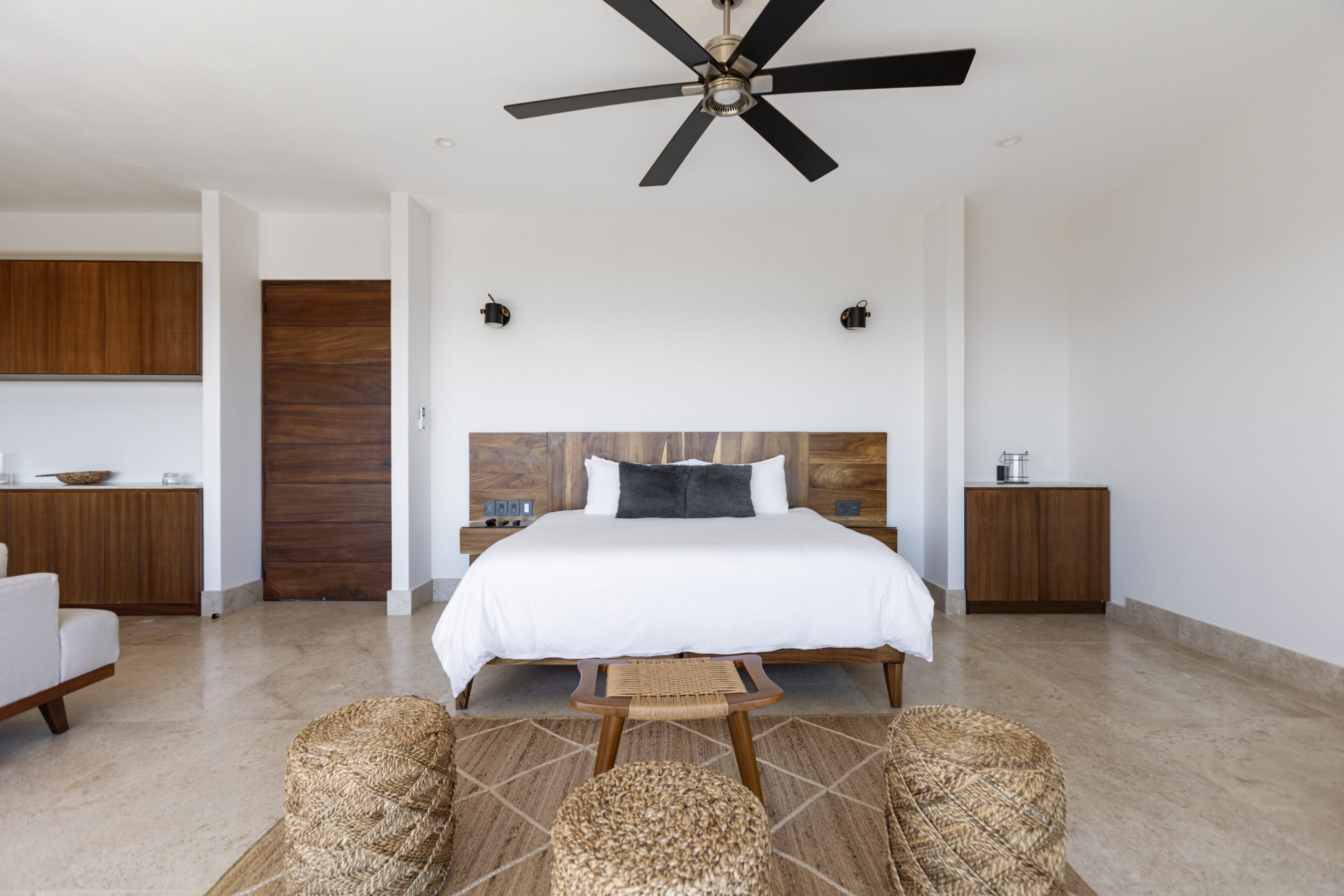 edroom with panoramic ocean views through large corner windows, light-colored curtains, and a cozy chair with a blanket.