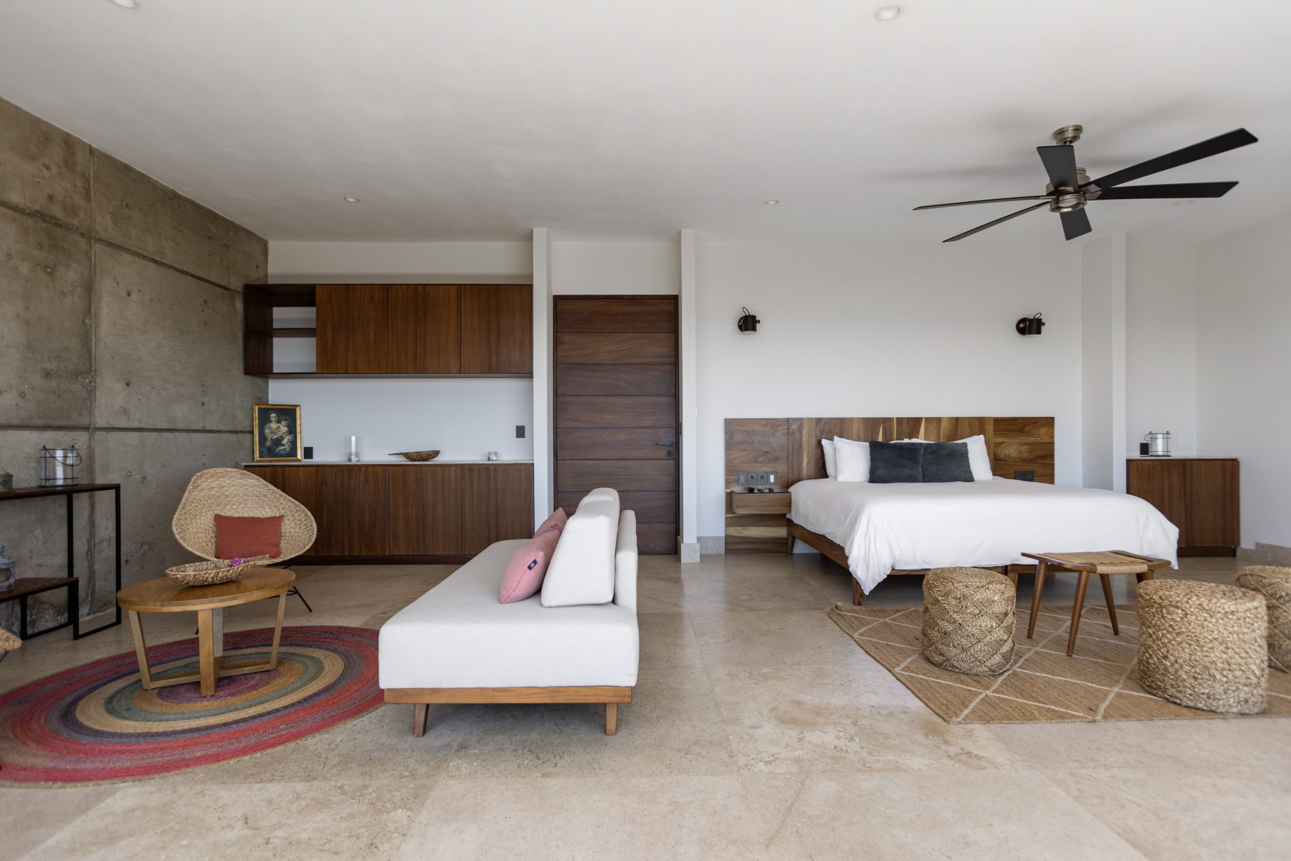 edroom with panoramic ocean views through large corner windows, light-colored curtains, and a cozy chair with a blanket.