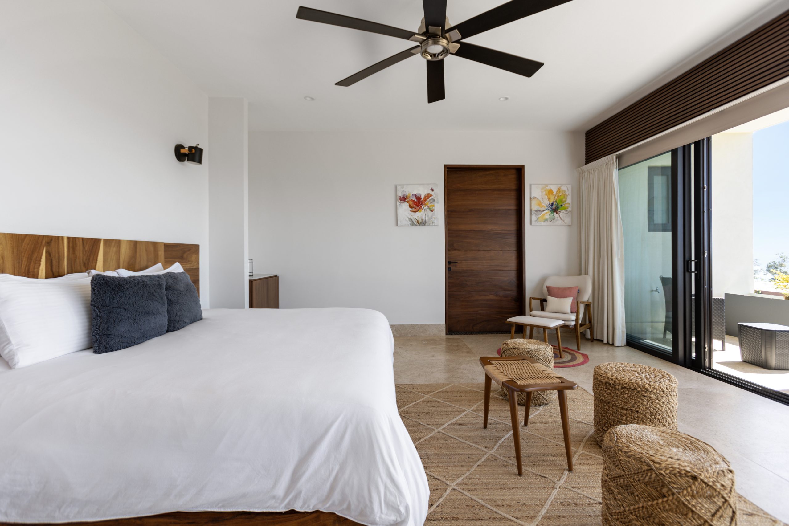 edroom with panoramic ocean views through large corner windows, light-colored curtains, and a cozy chair with a blanket.