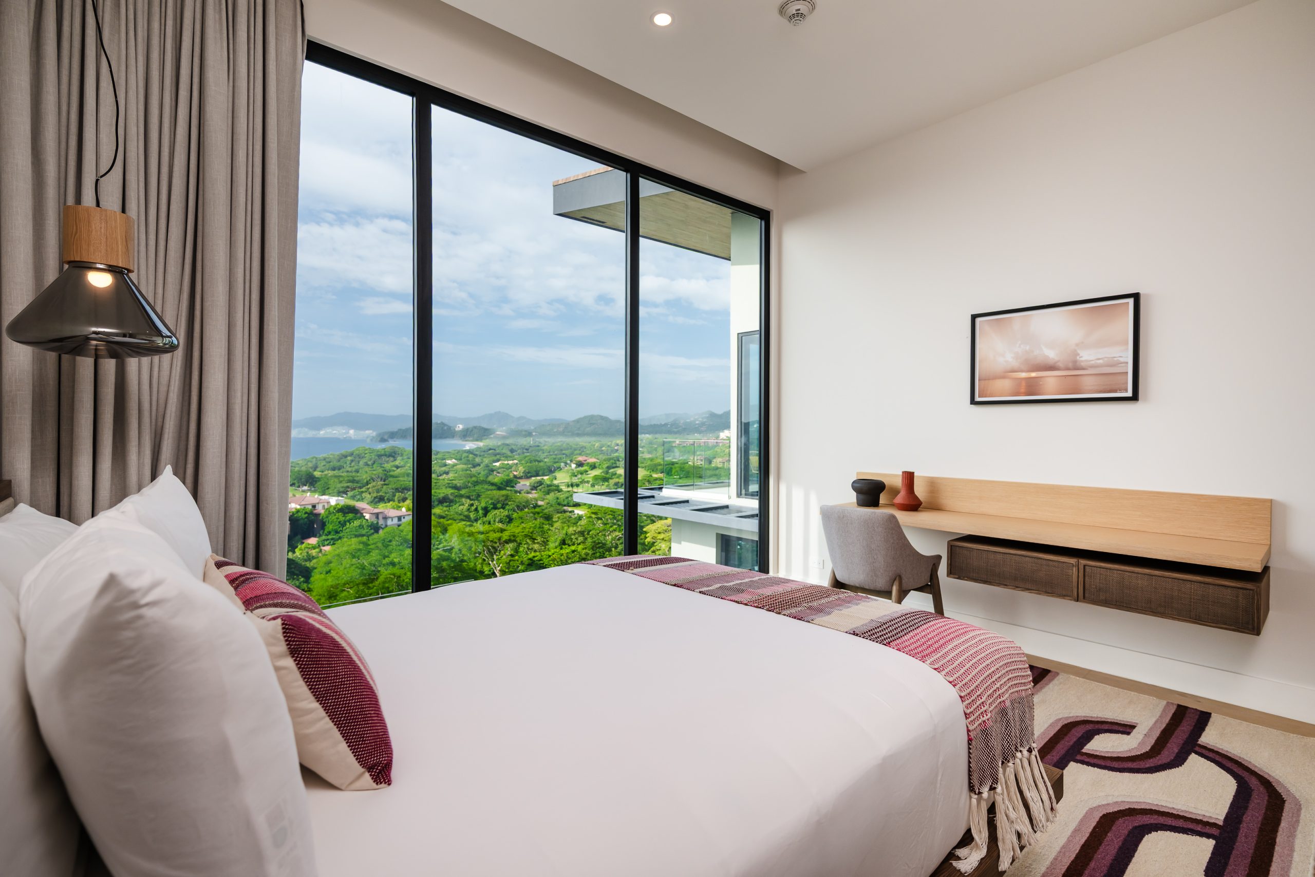 Luxury bedroom with floor-to-ceiling windows overlooking lush greenery and ocean views at the Reserva Conchal penthouse in Costa Rica