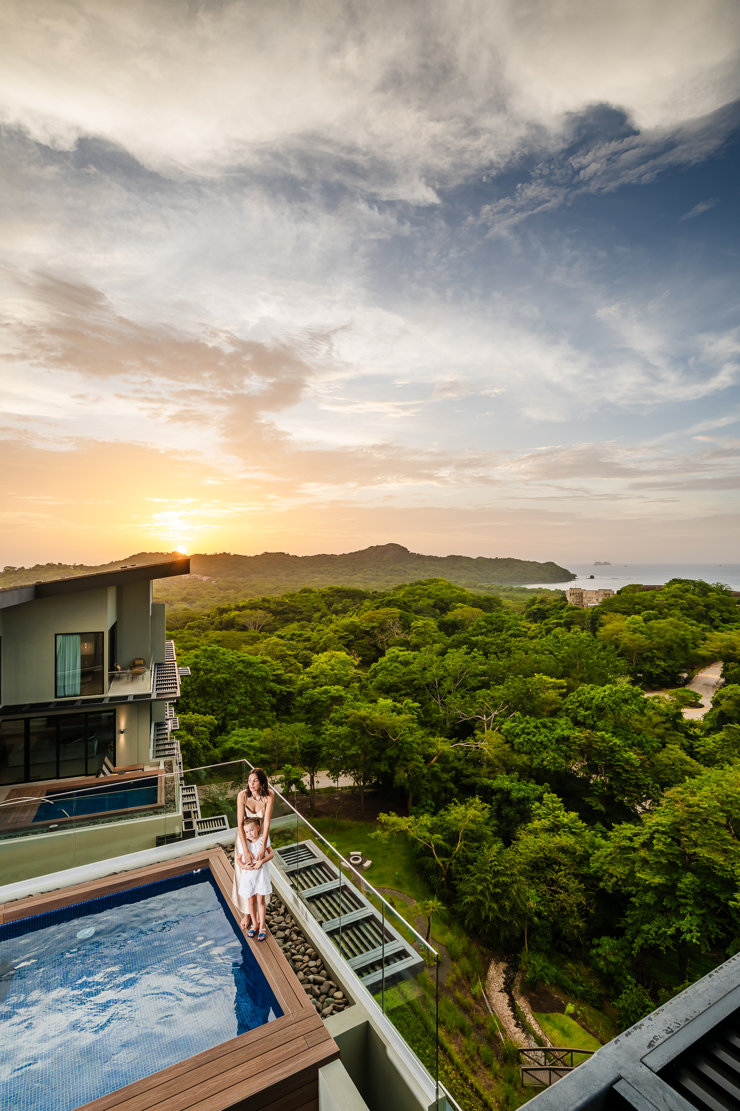 Woman relaxing by the private penthouse pool at Reserva Conchal, with panoramic sunset views of the Pacific Ocean and tropical forest.
