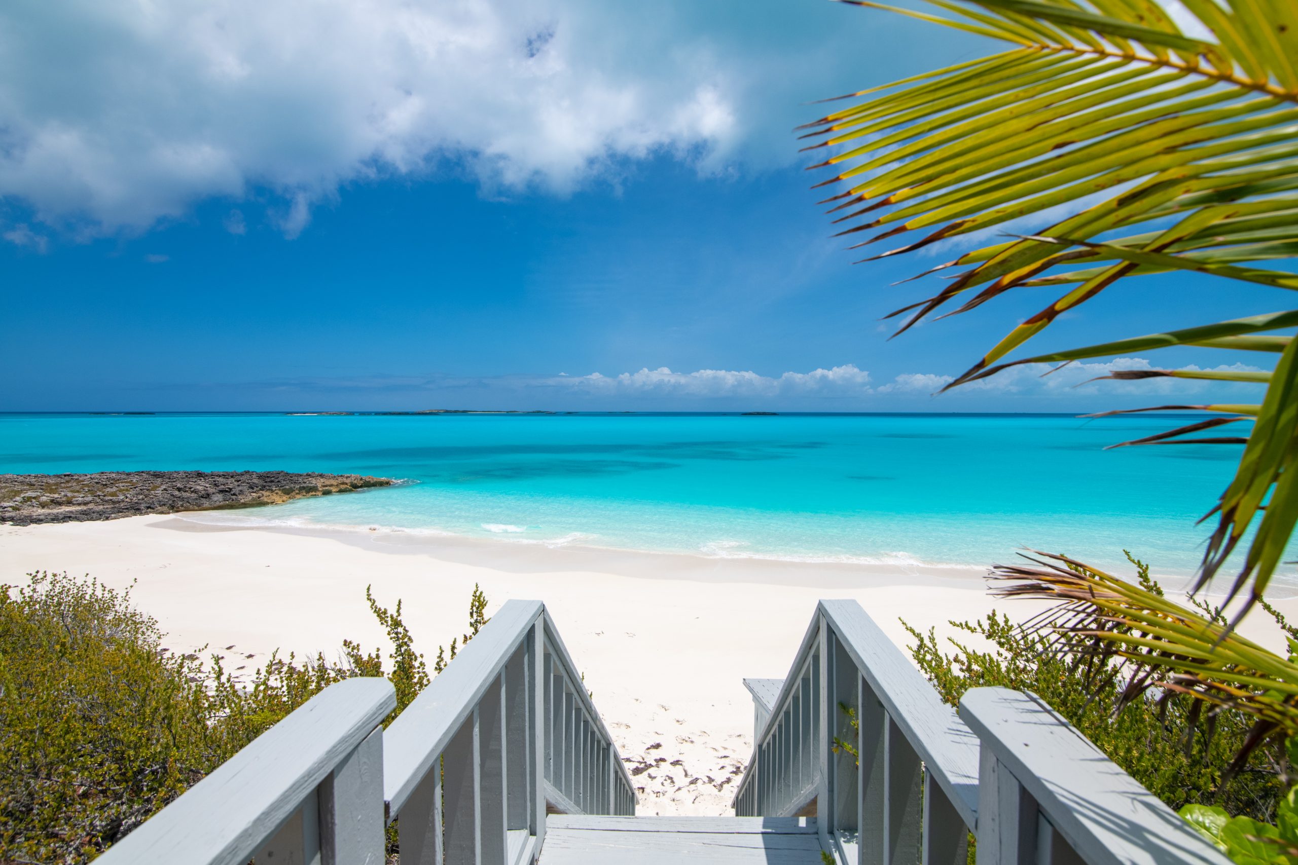 Stairs leading to a secluded white-sand beach and turquoise ocean in Little Exuma, Bahamas